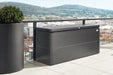 LoungeBox steel outdoor storage box in metallic dark grey finish, on a modern balcony overlooking stunning scenery