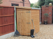 Small wooden tool shed with closed single door, viewed from the left side.