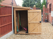 Small wooden tool shed with open single door, viewed from the left side. 