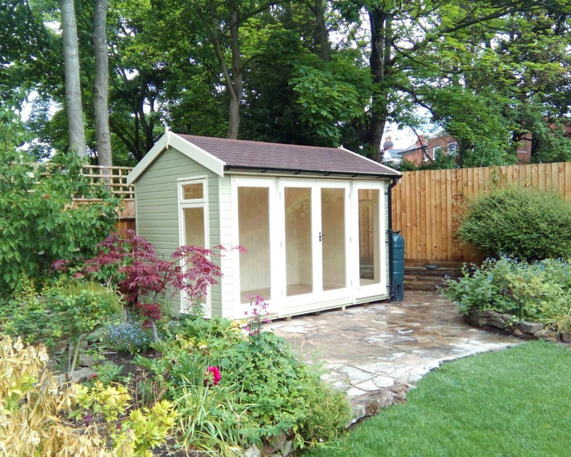 A traditional styled garden room with a pitched roof, situated in a garden setting, with large windows and double doors.
