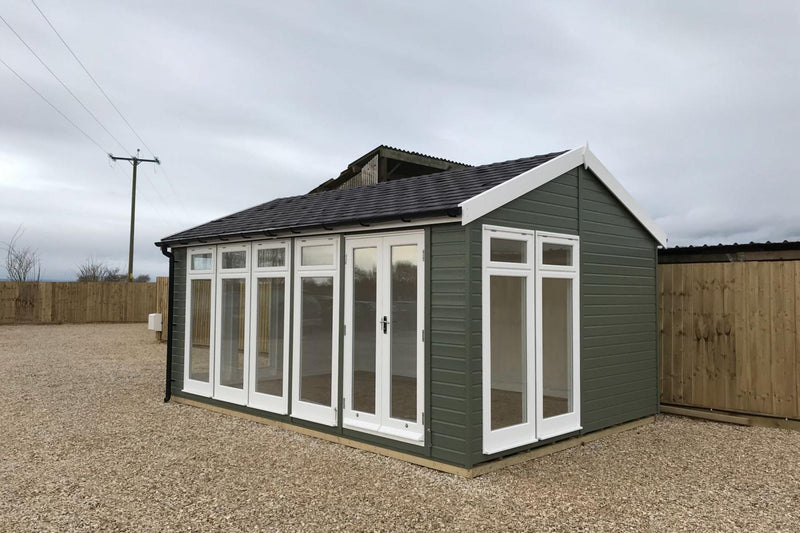 A traditional styled garden room with a pitched roof, situated outdoors, with a lot of windows and a set of double doors.