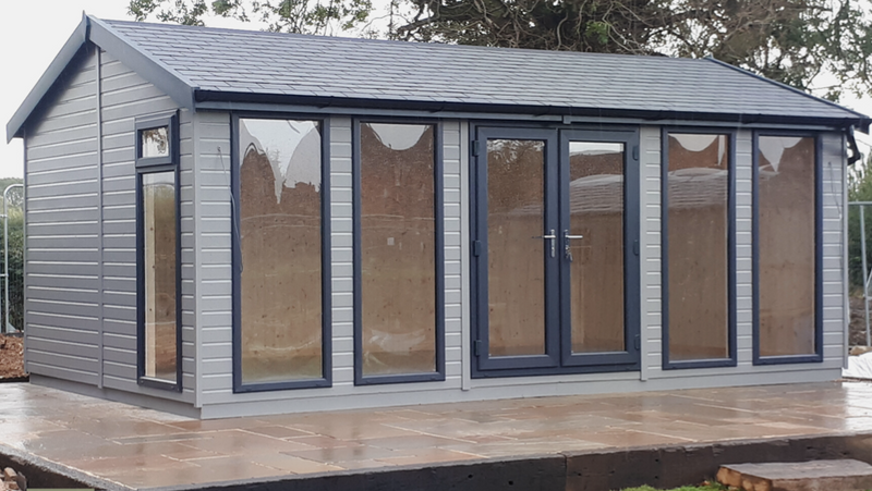 A traditional styled garden room with a pitched roof and large windows, presented in a grey color.